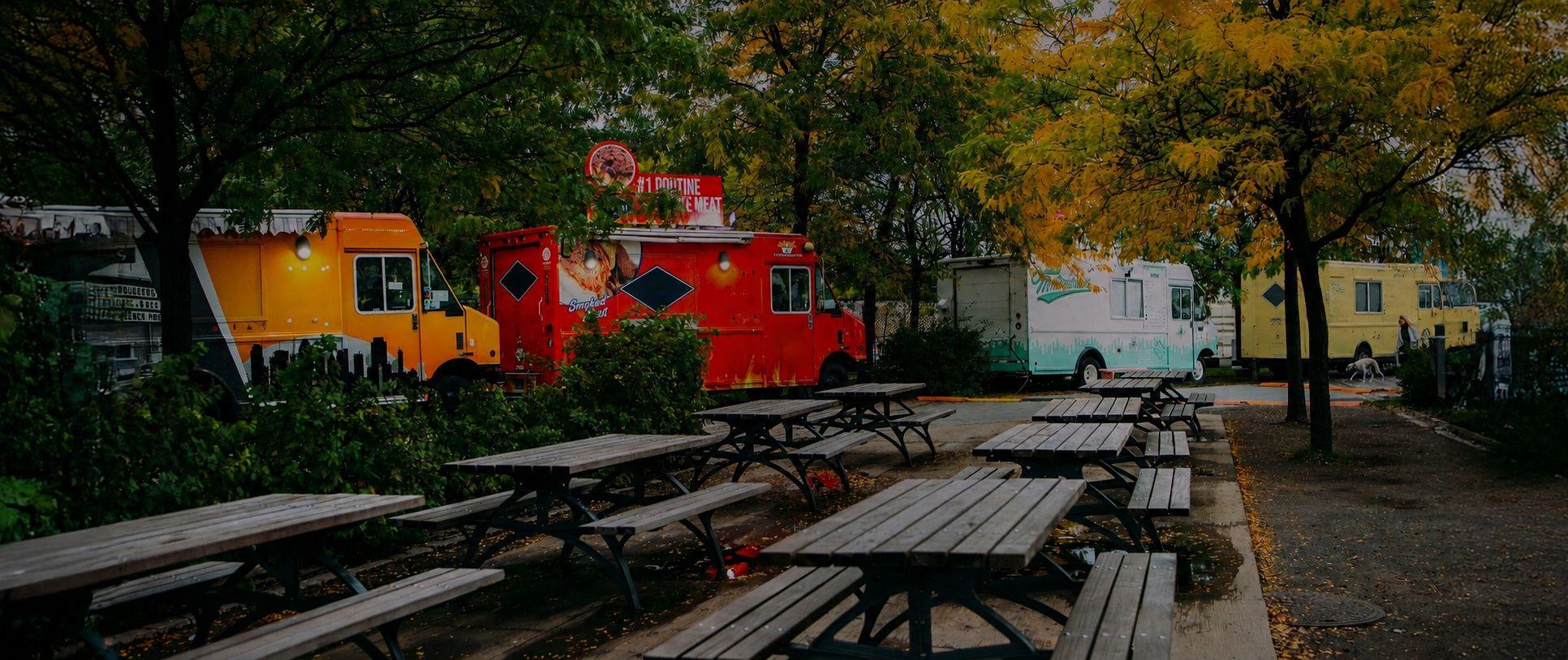 Food trucks lined up beside rows of picnic tables under the trees
